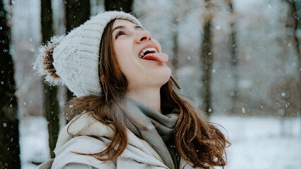 Portrait of woman catching snowflakes with tongue out in winter forest. Concept: winter magic...