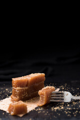 Dulce pasta de gelatina de membrillo dorado con sésamo molido y un tenedor sobre una placa de madera negra