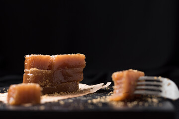 Dulce pasta de gelatina de membrillo dorado con sésamo molido y un tenedor sobre una placa de madera negra