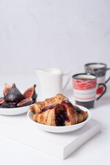 Desayuno con croissants, café y mermelada de higos sobre una mesa con fondo blanco