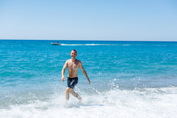 Attractive young man with a beautiful body in shorts walks along the sandy seashore and enjoying summer vacation