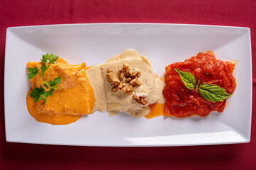 A Trio of Large Ravioli on a plate with three types of sauce.