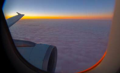view of sea of clouds at sunset out of airplane window seat window orange sunset with pink and...