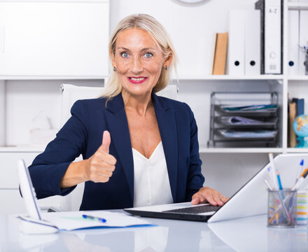 Confident smiling businesswoman in modern office showing thumbs up