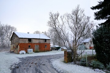Red brick barn standing by road in snowy winter scenery.