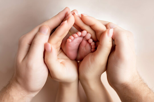 Little feet of a newborn baby girl in the hands of father and mother on a pink background. baby feet in parental hands
