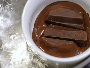 melting dark chocolate in white cup in boiling water pot, close up