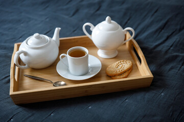 Interior and home cosiness concept. Top view. A cup of tea, a teapot with herbal tea, sugar bowl on a wooden tray on the bed