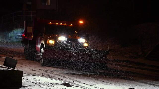 A nighttime slow motion view of a public works salt truck treats a snowy residential road during a snowstorm. Shot at 60fps.  	