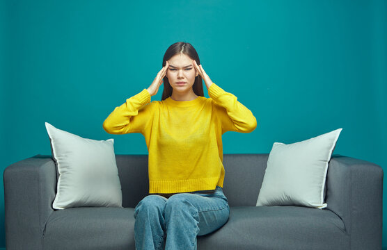 Sick stressed young girl suffer premenstrual migraine, feel unbearable headache massaging temples sitting on couch
