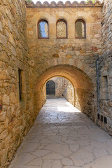 Fototapeta premium Pals, street with stone buildings, arch across the street with reflection in the windows, in the old town of Pals, catalonia, Girona, northeastern spain.