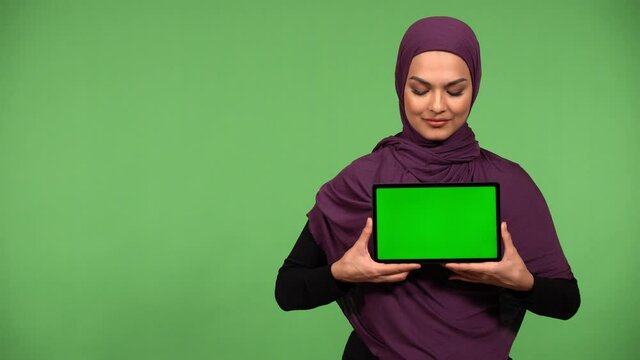 A young beautiful Muslim woman shows a tablet with green screen to the camera with a smile - green screen background