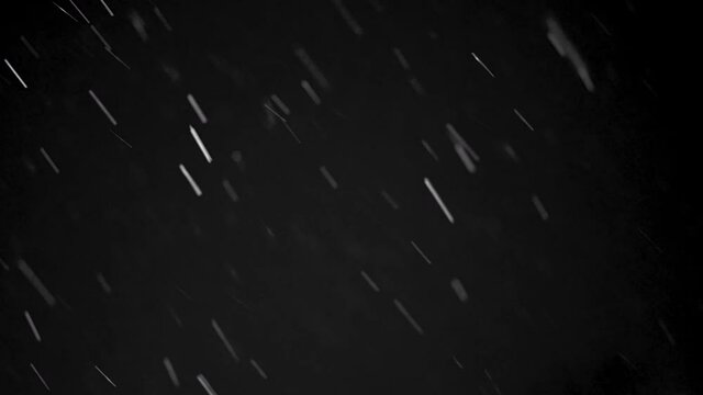 A slow motion view of snowflakes falling over a dark night sky. Good for keying over video.  	