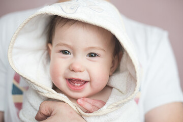 A pretty laughing baby in a white towel in his father's arms