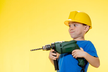 Cute boy in a construction helmet with a drill in his hands