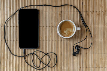 a cup of coffee and smartphone with headphones on a beige bamboo surface, top view, mock up