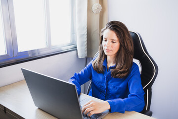 Young woman wearing a blue long sleeve shirt working on the notebook. Studying on the laptop.