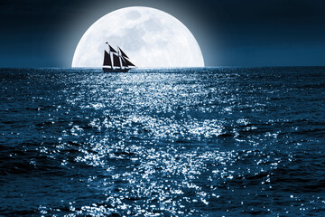 Very large full blue moon rises over this ocean scene as a sailboat quietly saiils in front of it...