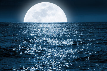 Very Large Full Blue Moon rises over a calm ocean scene.