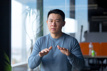 Portrait of a serious and angry employee, looking at the camera and gesturing with his hands, Asian...