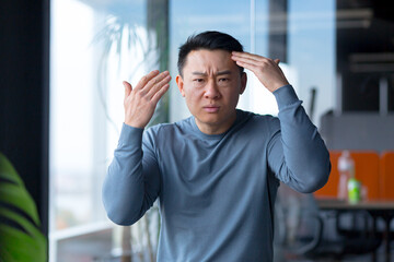 Portrait of a serious and angry employee, looking at the camera and gesturing with his hands, Asian...