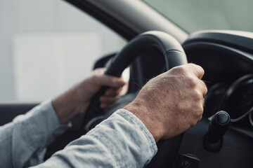 Close up and portrait of old and retired man holding steering wheel with his hands driving and...