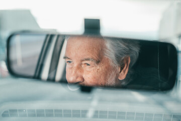 Portrait of one old pensioner man driving and enjoying his new car. Rear view mirror.