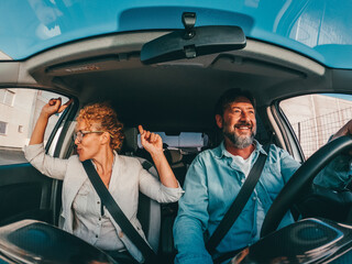 Couple of happy people dancing and singing in the car driving and traveling with a vehicle in the...
