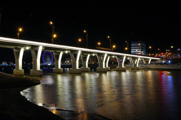 The cityscape with the bridge over the bay in Cheboksary with illumination and evening city lights.