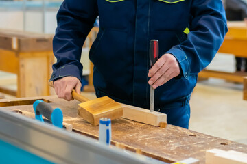 Professional man carpenter using chisel and hammer to carve wood on workbench at workshop: close...