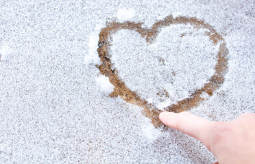 Top view, closeup hand drawing imperfect heart shape on icy snow covering a floor on a cold-weather day. Symbol of love in winter season. Romantic outdoor concept for Valentine's day with copy space.T