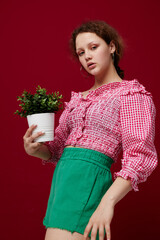 Young woman in pink blouse is posing with a plant in white pot close-up