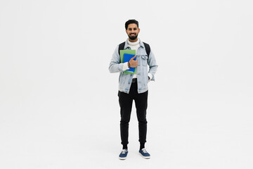 Smiling indian student standing with textbooks and backpack on white background