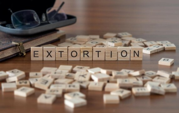 extortion concept represented by wooden letter tiles on a wooden table with glasses and a book
