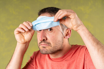 A man  looking under a surgical blue mask in a green background. He Looks with suspicion and fear...