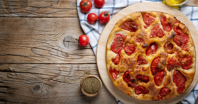 Bari-style focaccia bread. Focaccia barese with cherry tomatoes, olive oil and oregano on wooden background, top view, space for text.