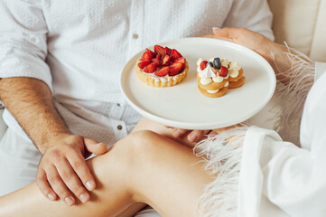 Obraz na płótnie Canvas happy couple having breakfast in bed with delicious cookies with strawberries on top