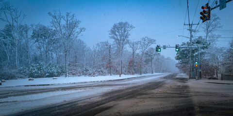 Snowstorm at the crossroads with green and red traffic lights. Empty paved street in the...