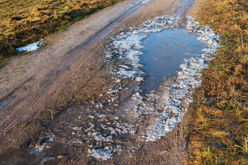 Melting ice and puddle on a country road in winter day