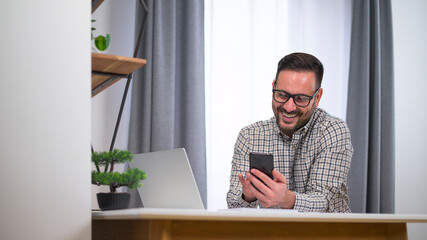 Smiling young manager working from home sending message to friend or coworker during break. Working at home during corona virus lock down