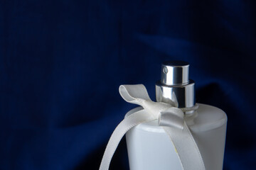 White bottle of perfume on a dark blue background. The perfume diffuser is decorated with a white...