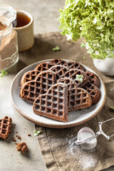 Heart-shaped chocolate waffles as Valentine's Day breakfast, sprinkled with powdered sugar
