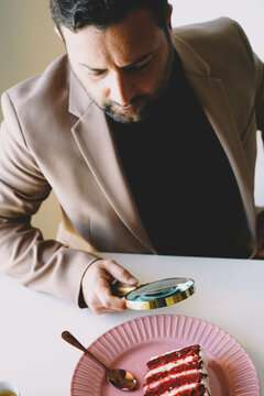 Hombre analizando un pastel de terciopelo rojo con una lupa
