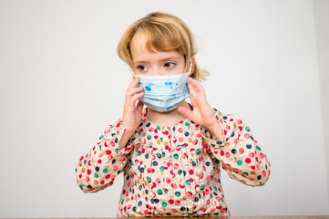 Portrait of cute blonde girl with medical face mask at home.