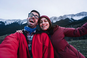 Beautiful couple of young adults taking selfie in the snow mountains - Happy hiker tourists traveling and exploring nature in winter