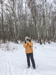 Fototapeta na wymiar Man with camera in winter forest. Photographer takes pictures of trees under snow. Leisure activity in cold season.