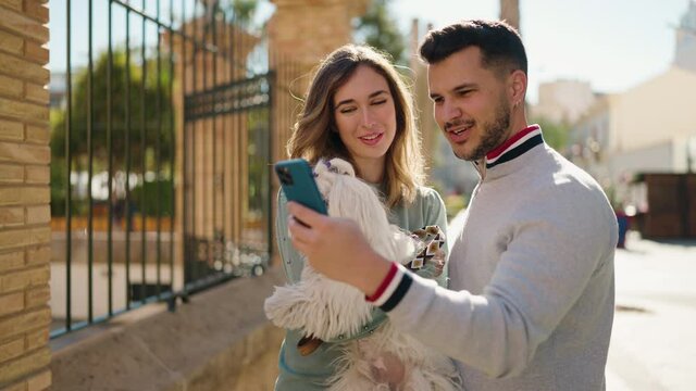 Young couple holding dog make selfie by the smartphone at street