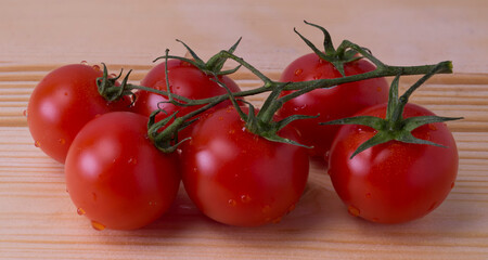 Bunch of red tomatoes with small drops of water, on light wooden table