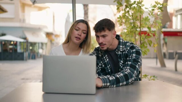 Young couple smiling confident using laptop at coffee shop terrace