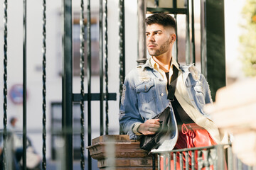 Caucasian model leaning on a fence with a distracted gaze